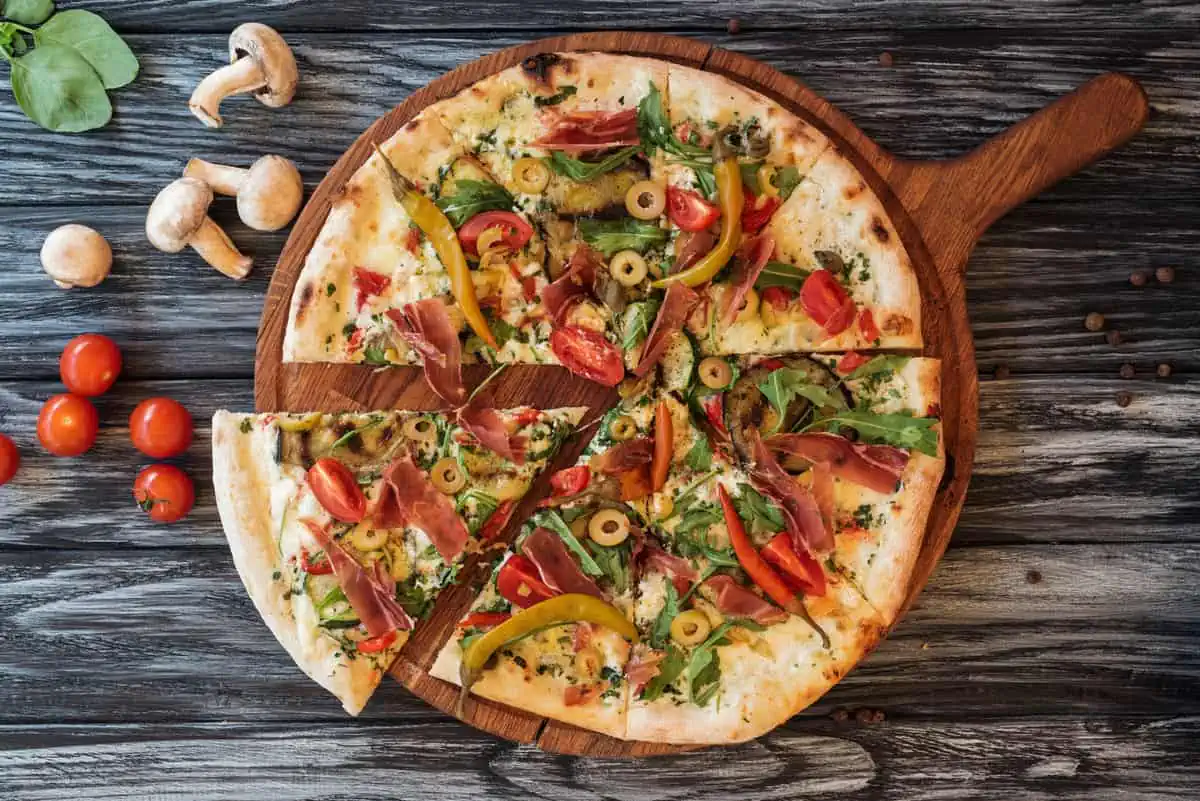 A gourmet pizza with a mix of vegetables and meat toppings, served on a rustic wooden table