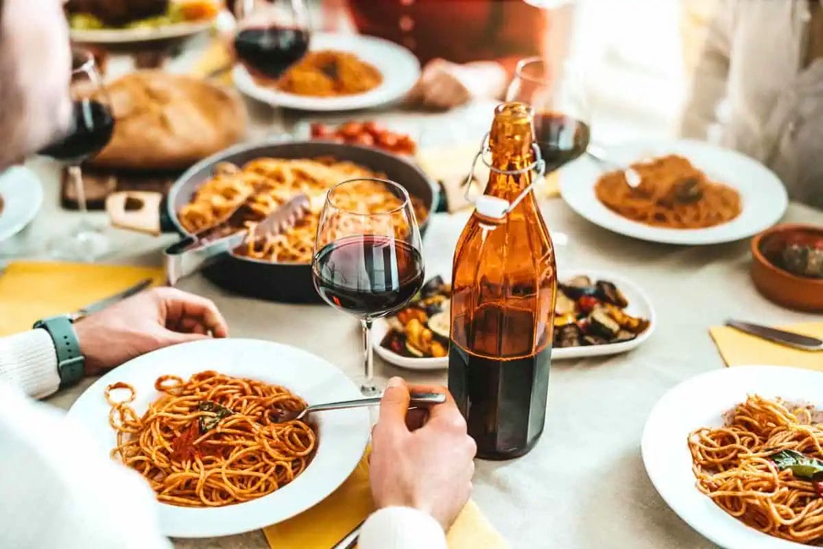 A group of friends sharing a pasta meal with a bottle of red wine on the table