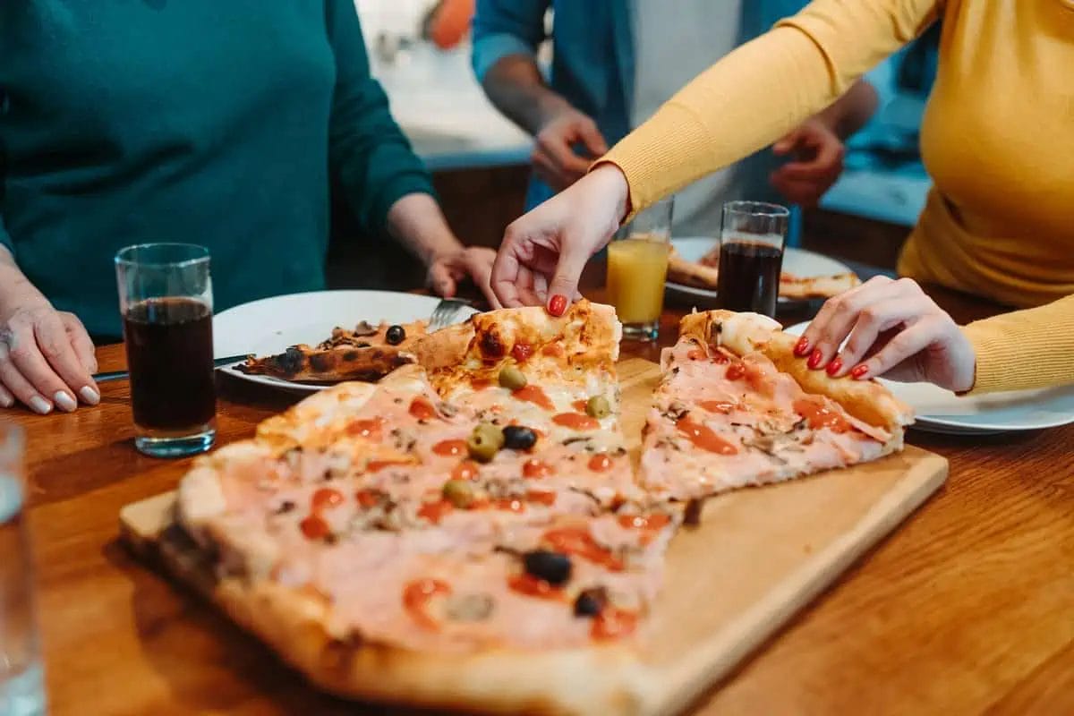 A group of people sharing a large, topped pizza at a social gathering