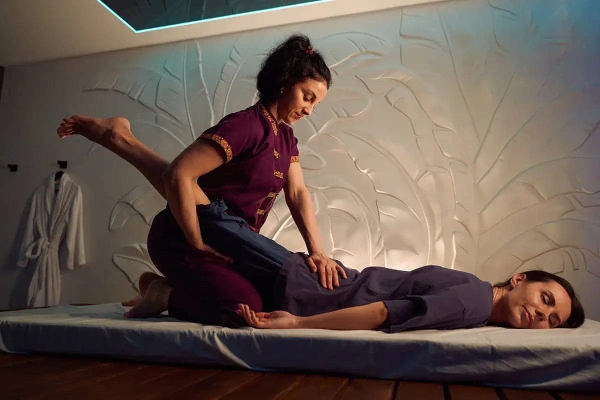 A massage therapist applying a leg stretch to a client on a mat in a modern wellness center