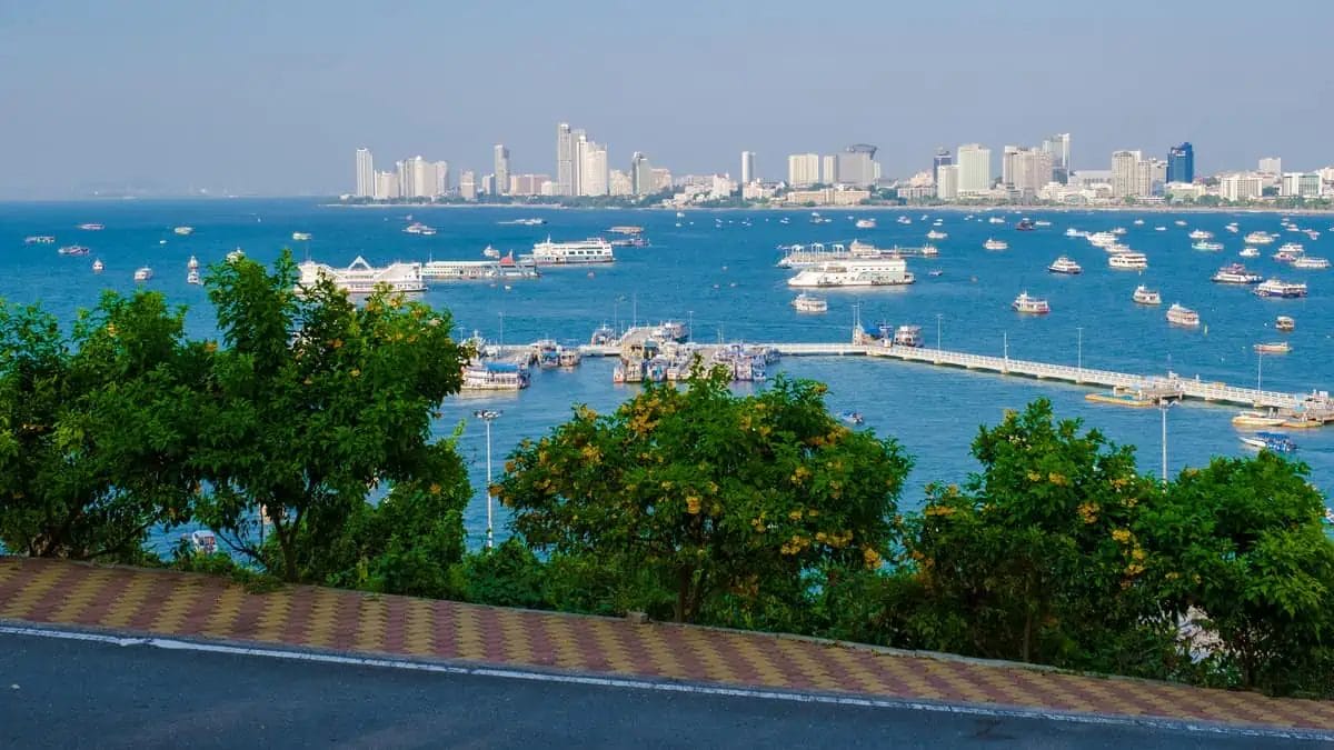 A panoramic view of Pattaya's coastline from a hilltop, showing boats in the bay and city skyline in the background.
