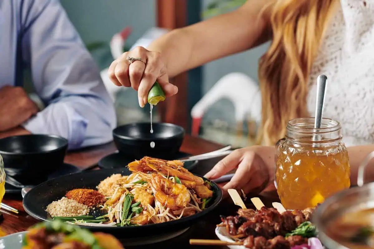 Discover the Best Thai Restaurants in Pattaya: A Culinary Guide 2 A person adding a splash of lime juice to a flavorful dish of shrimp Pad Thai, enhancing the taste with a citrusy zing