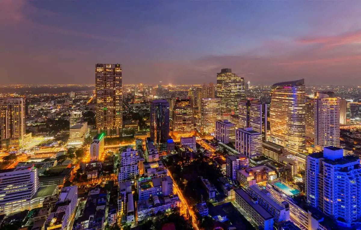 Aerial view of Silom district in Bangkok at dusk, with illuminated high-rises and a colorful sky