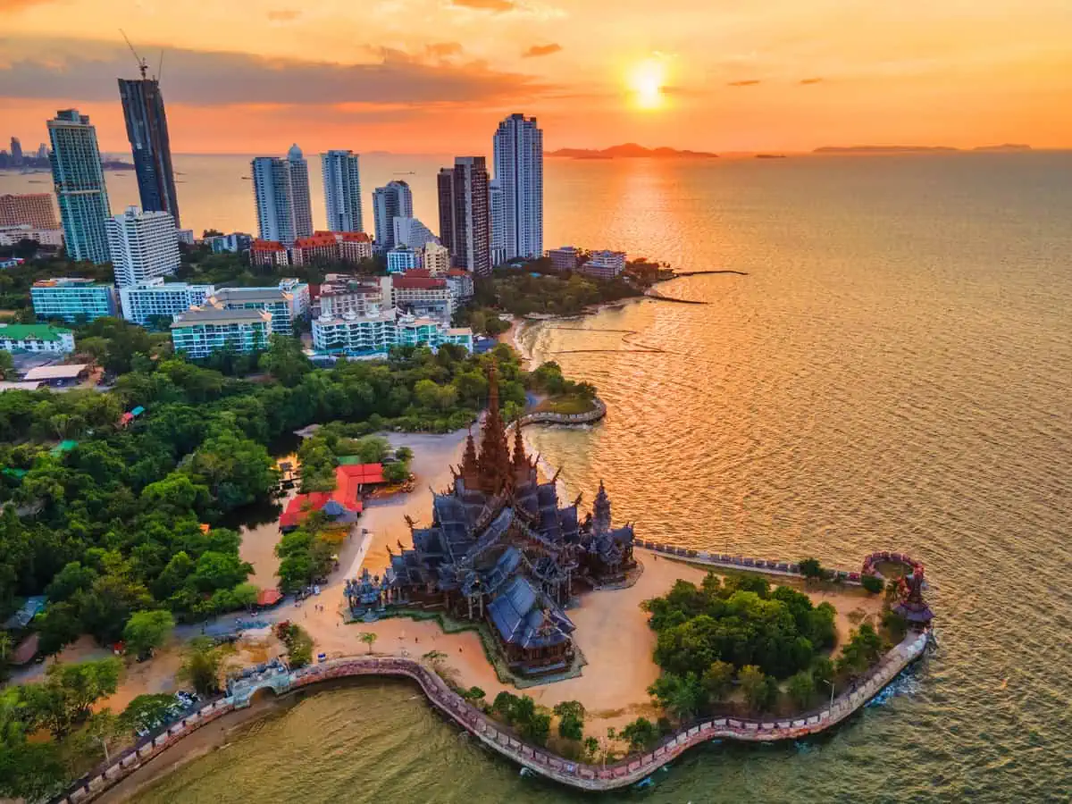 Aerial view of the Sanctuary of Truth, a large wooden temple in Pattaya, Thailand, at sunset with the city skyline and ocean in the background