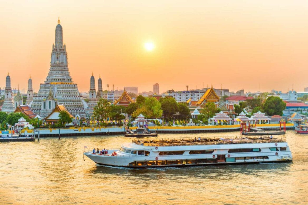 Dawn at the stunning Wat Arun temple beside the Chao Phraya River with boats and a radiant sunset, exemplifying Bangkok sightseeing attractions