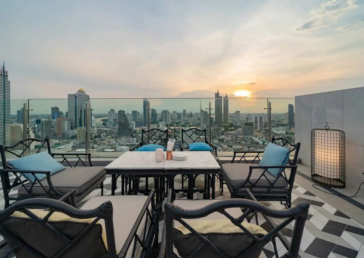 Elegant rooftop dining setup ready for guests, with stylish furniture and place settings, overlooking a panoramic cityscape at dusk