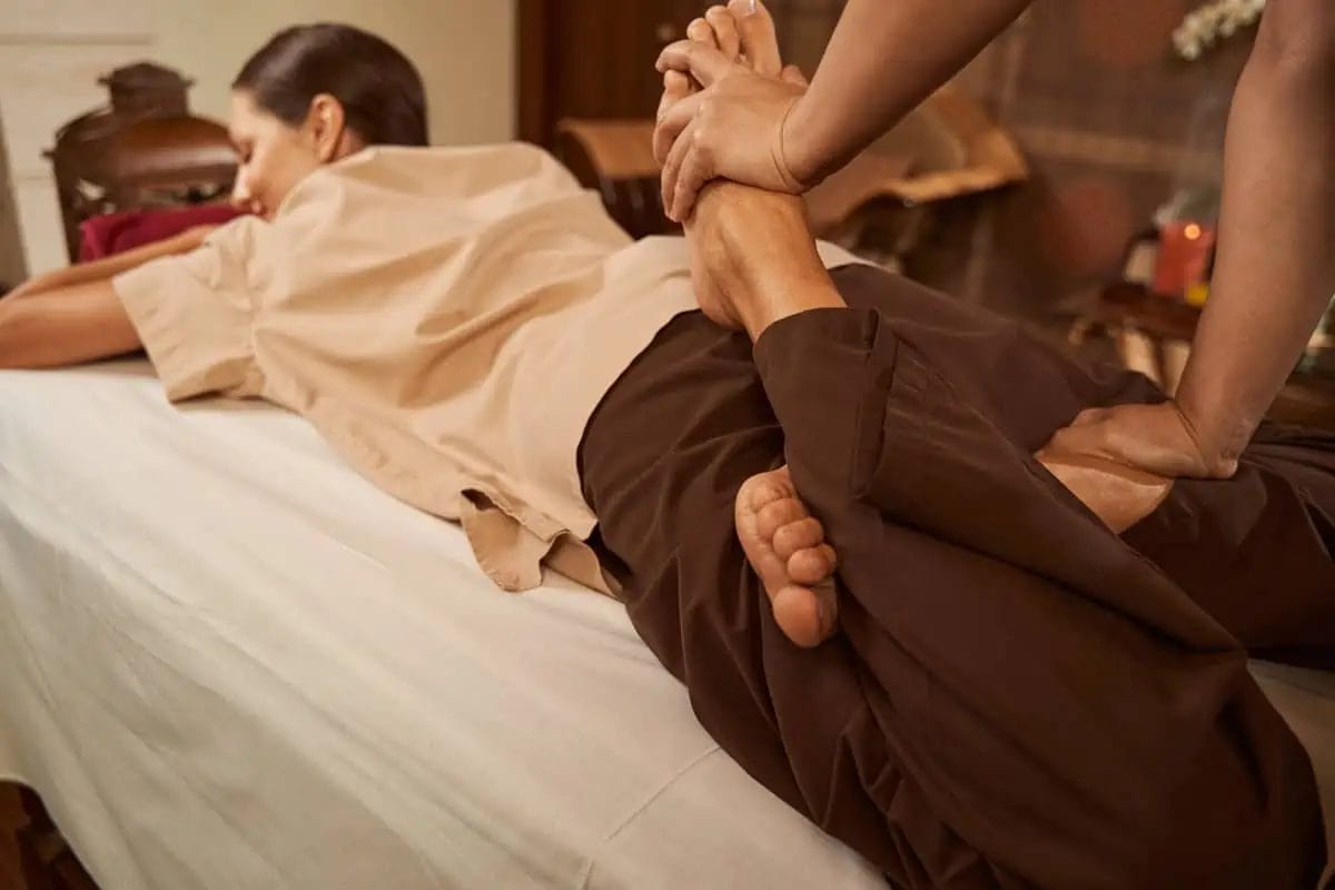 Practitioner executing a lower leg stretch on a client during a traditional Thai massage