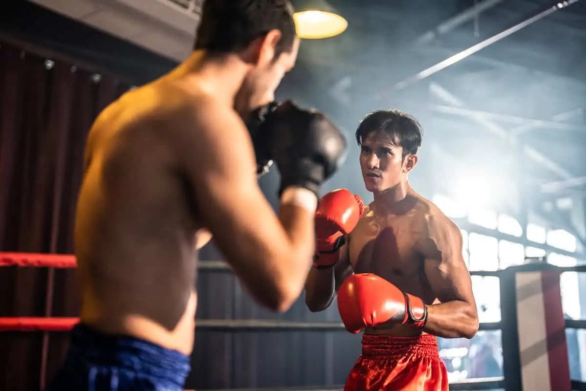 Two male Muay Thai boxers spar in a ring, practicing defensive and offensive moves with focus and determination