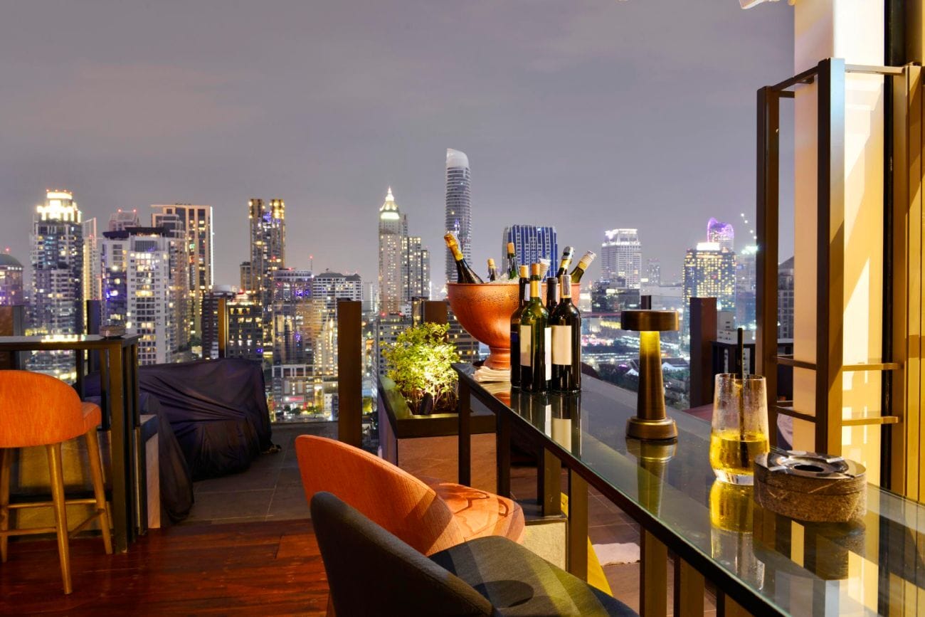 Sky High Delights: 30 Top Rooftop Bars in Bangkok for Foodies and Drink Connoisseurs 2 View of Bangkok from a rooftop bar, showcasing the cityscape against a blue sky, illuminated by city lights.